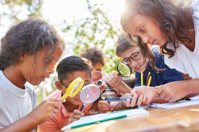 Students looking closely at something they are investigating with a magnifying glass.